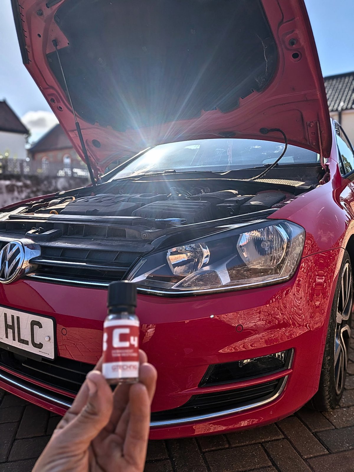 Person holding car maintenance product in front of open red Volkswagen Golf with bonnet raised